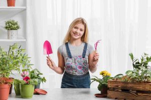 Young girl holding essential tools for indoor plant owners surrounded by indoor plants.